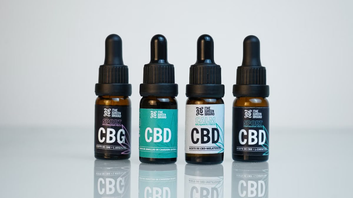 Four CBD and CBG oil bottles in a row on a reflective surface, showcasing product branding.
